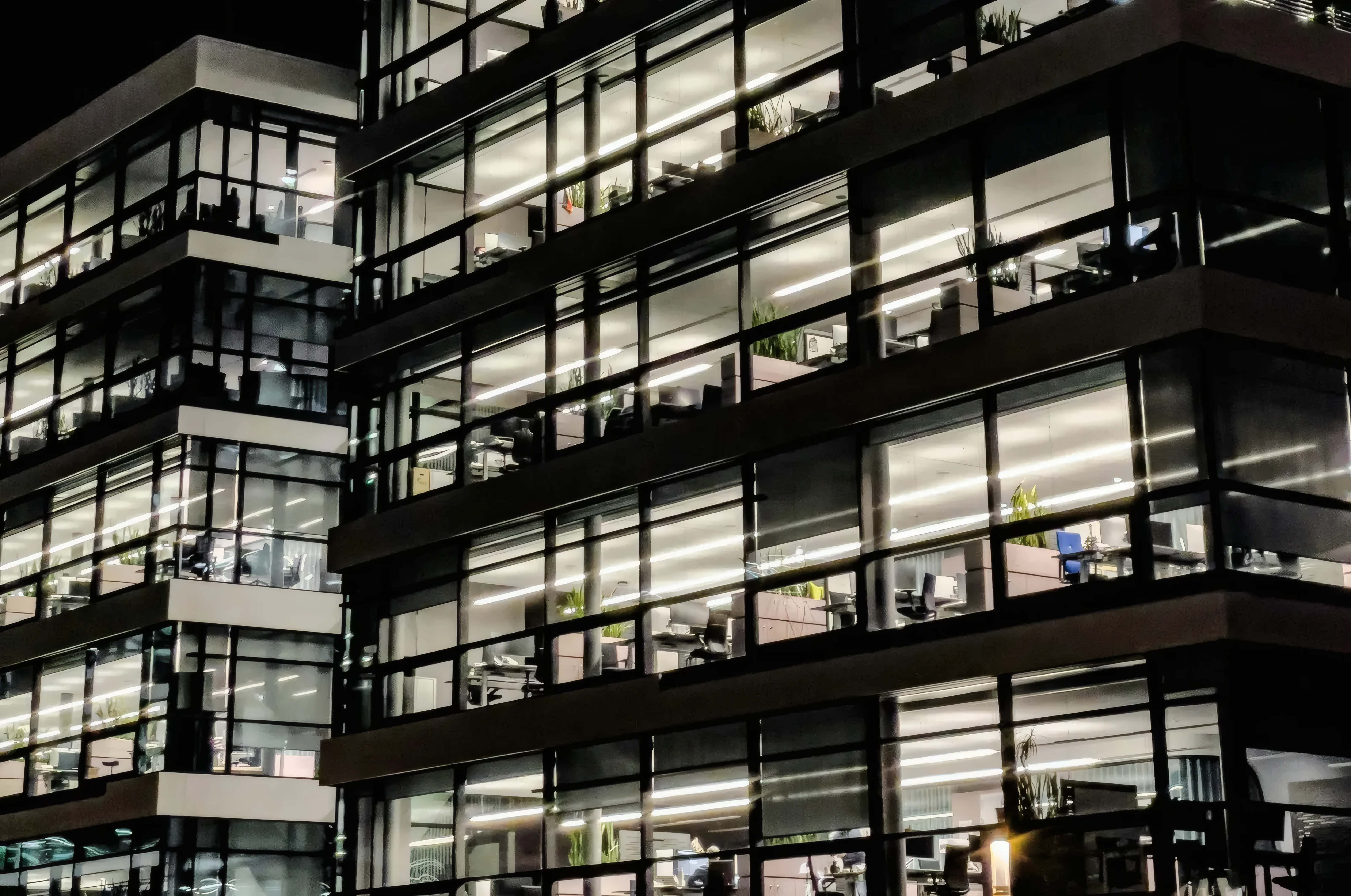 Office building at night with every floor lit behind its glass facade